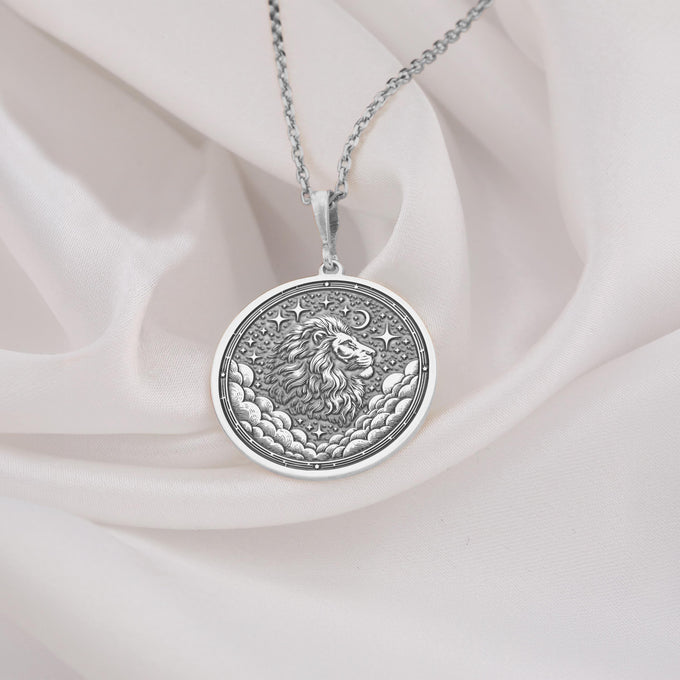 Silver circular pendant featuring a detailed lion face with a full mane, surrounded by celestial patterns and clouds. The pendant is attached to a silver-toned chain and shown in a front view.
