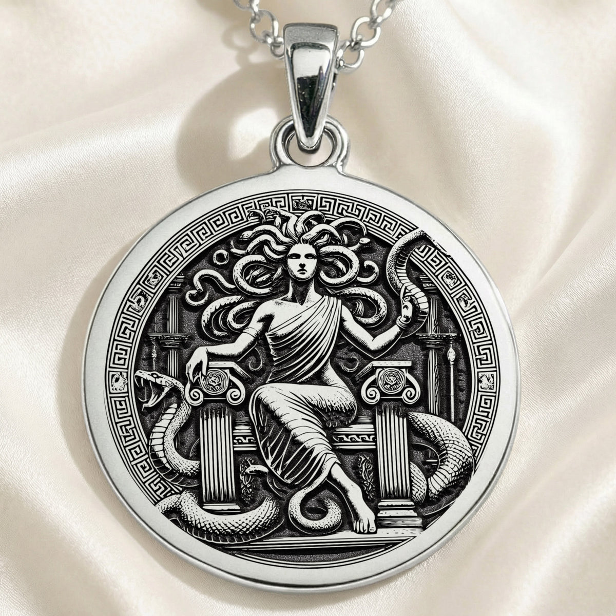 Silver pendant featuring a detailed Medusa Gorgon motif with intricate details, presented from a slightly elevated angle. The pendant is circular and has a textured surface finish, hanging from a delicate silver chain.
