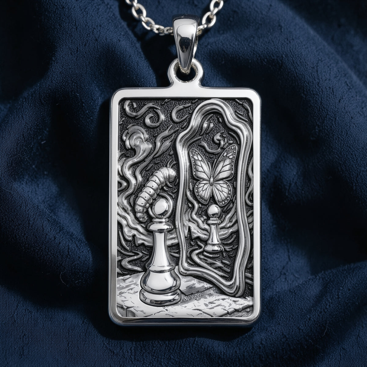A silver toned rectangular pendant featuring intricate line art. The pendant is worn on a chain and arranged with various colored, faceted gemstones on a dark surface.