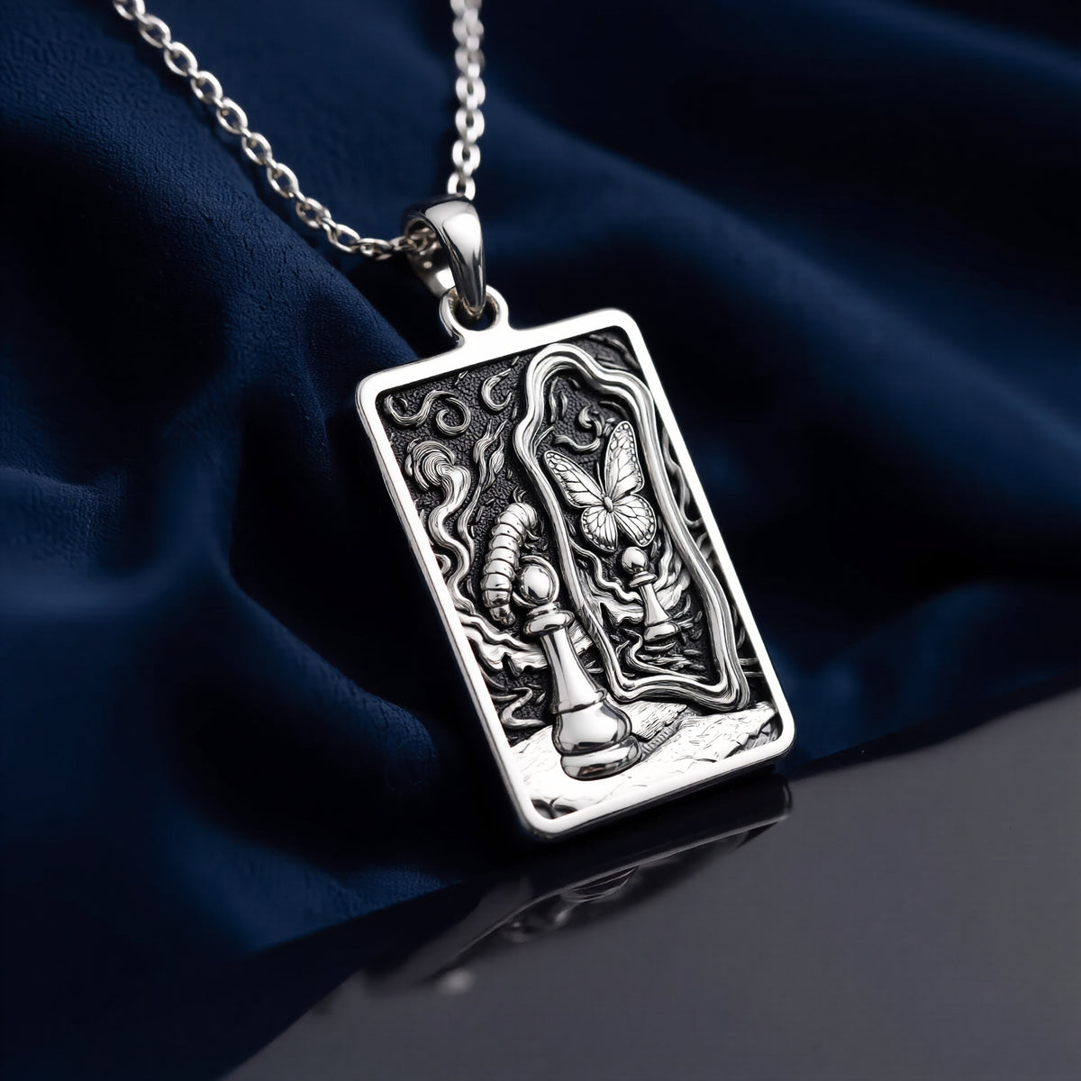 Silver toned rectangular pendant with detailed line art design. This necklace is displayed on black fabric alongside several faceted gemstones. - View 8