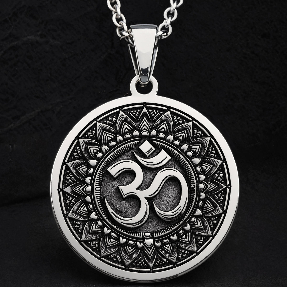 Silver circular pendant featuring an ornate border design around the central Om motif. The pendant is suspended from a silver chain, presented in a clear, frontal view.