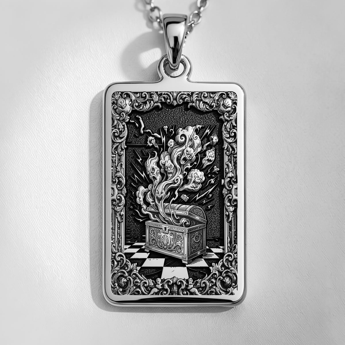 Silver rectangular pendant necklace featuring an ornate, detailed frame design with intricate scrollwork. The pendant is attached to a silver chain and displayed among faceted gemstones.