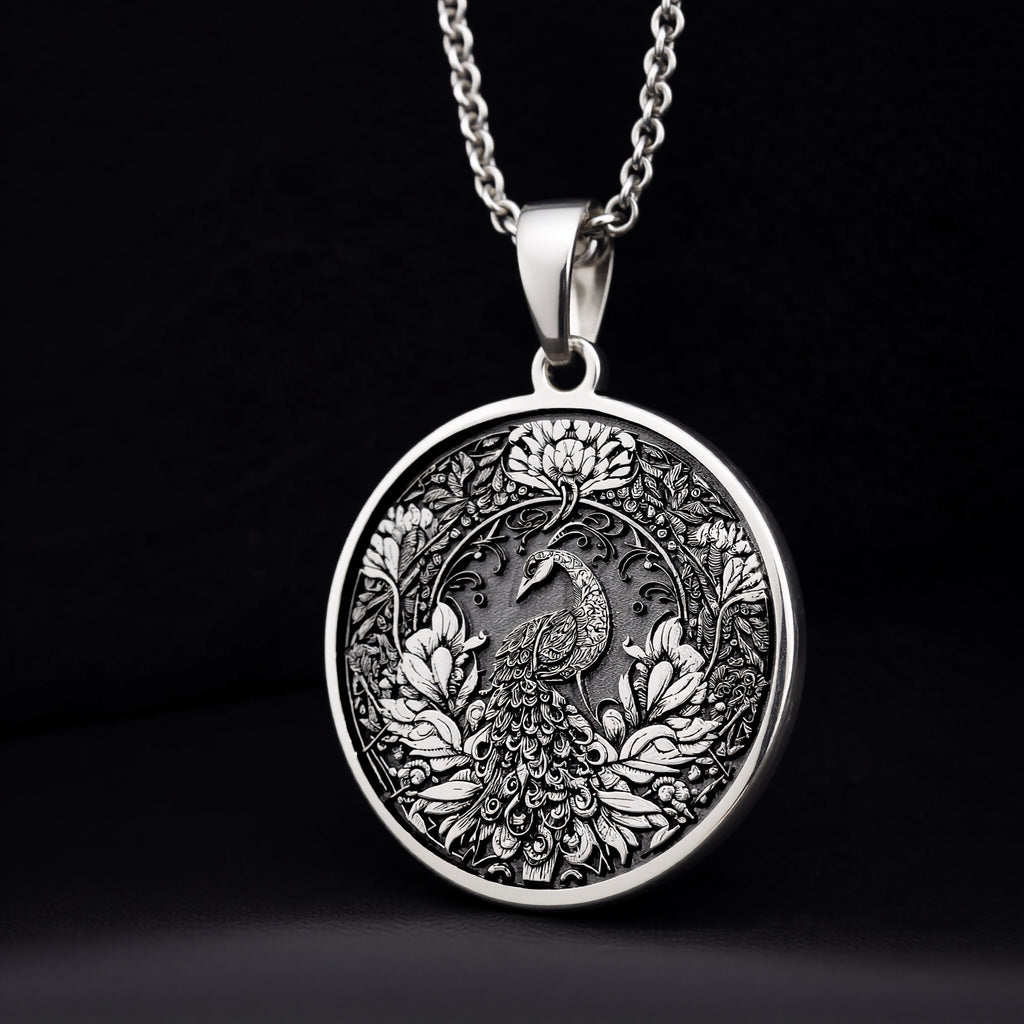 Silver pendant featuring an intricate peacock feather bird design with detailed filigree work. The pendant has a textured, antique finish and is shown from a slight angle against a dark background. A delicate silver chain is visible.