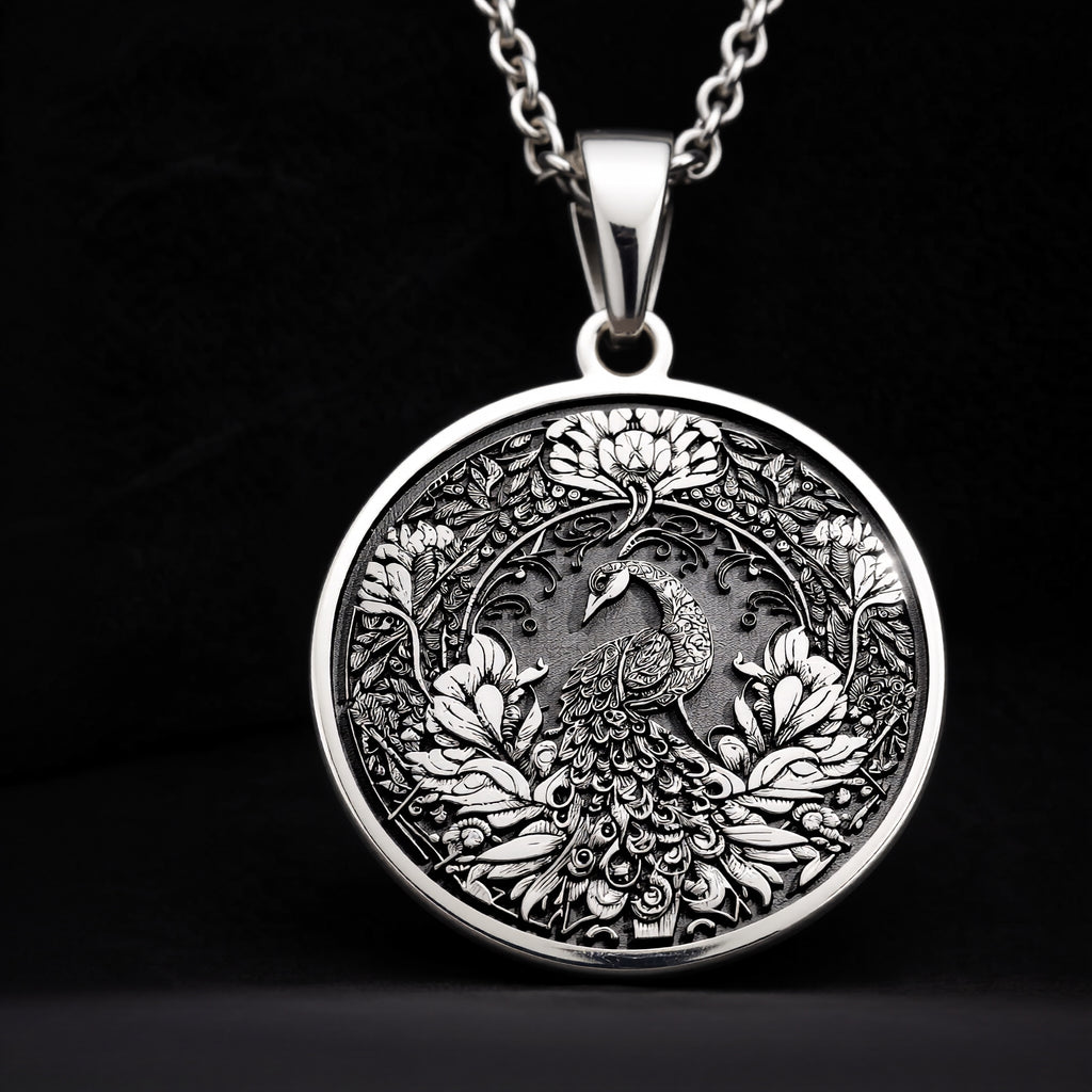 Silver colored circular pendant featuring an intricate embossed design of a peacock surrounded by detailed foliage. The pendant is attached to a silver-toned chain and displayed on a textured surface. - View 8