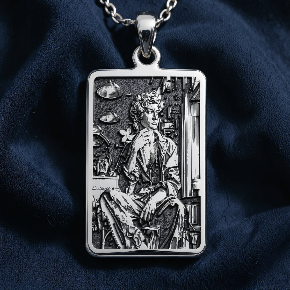 Silver rectangular pendant with fine engraving depicting a classical scene. The pendant is attached to a silver chain and displayed alongside various gemstones on a black surface.