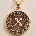 Front studio view of 14K solid yellow gold Sagittarius zodiac glyph (♐) medallion pendant framed by a botanical laurel wreath border.
