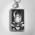 Silver rectangular pendant necklace featuring an engraved design of a frog with surrounding leaves. The metal has a bright, reflective finish and is displayed on a black background with various colored faceted stones.